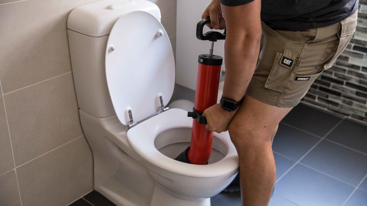A man providing plumbing service in a city, fixing a toilet with a red hose.